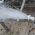 Metal pipe expelling water forcefully onto concrete, illustrating plumbing issues with high pressure, related to burst pipes.