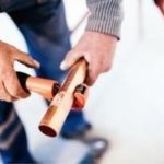 Close-up of hands using a pipe cutter on a copper pipe for plumbing, illustrating craftsmanship in repiping.