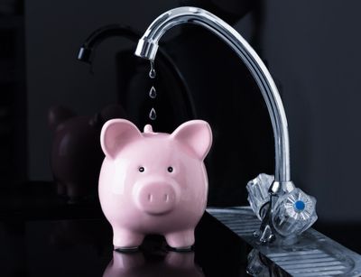Leaking faucet dripping water above a pink piggy bank, illustrating the financial impact of a dripping faucet on homeowners.