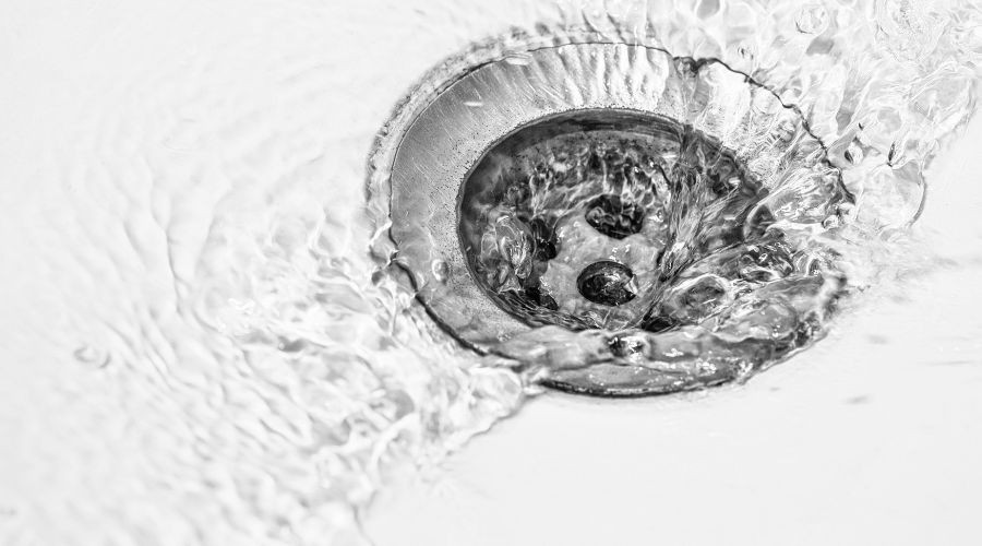 Circular metal drain with swirling water illustrating plumbing and drainage services from Guardian Plumbing and Drain.